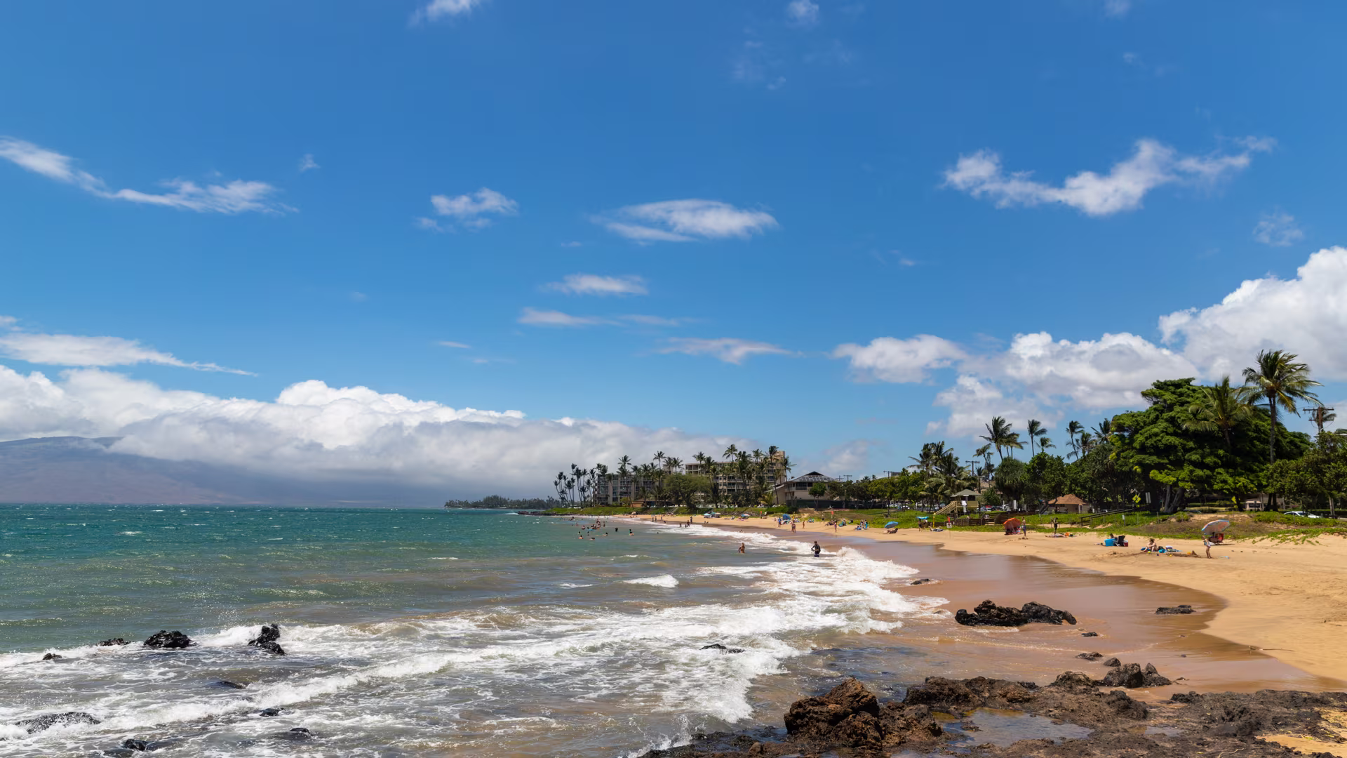 Kamaole Beach Park II, a long golden sand beach in Kihei, Maui, with lava rock and the West Maui Mountains beyond