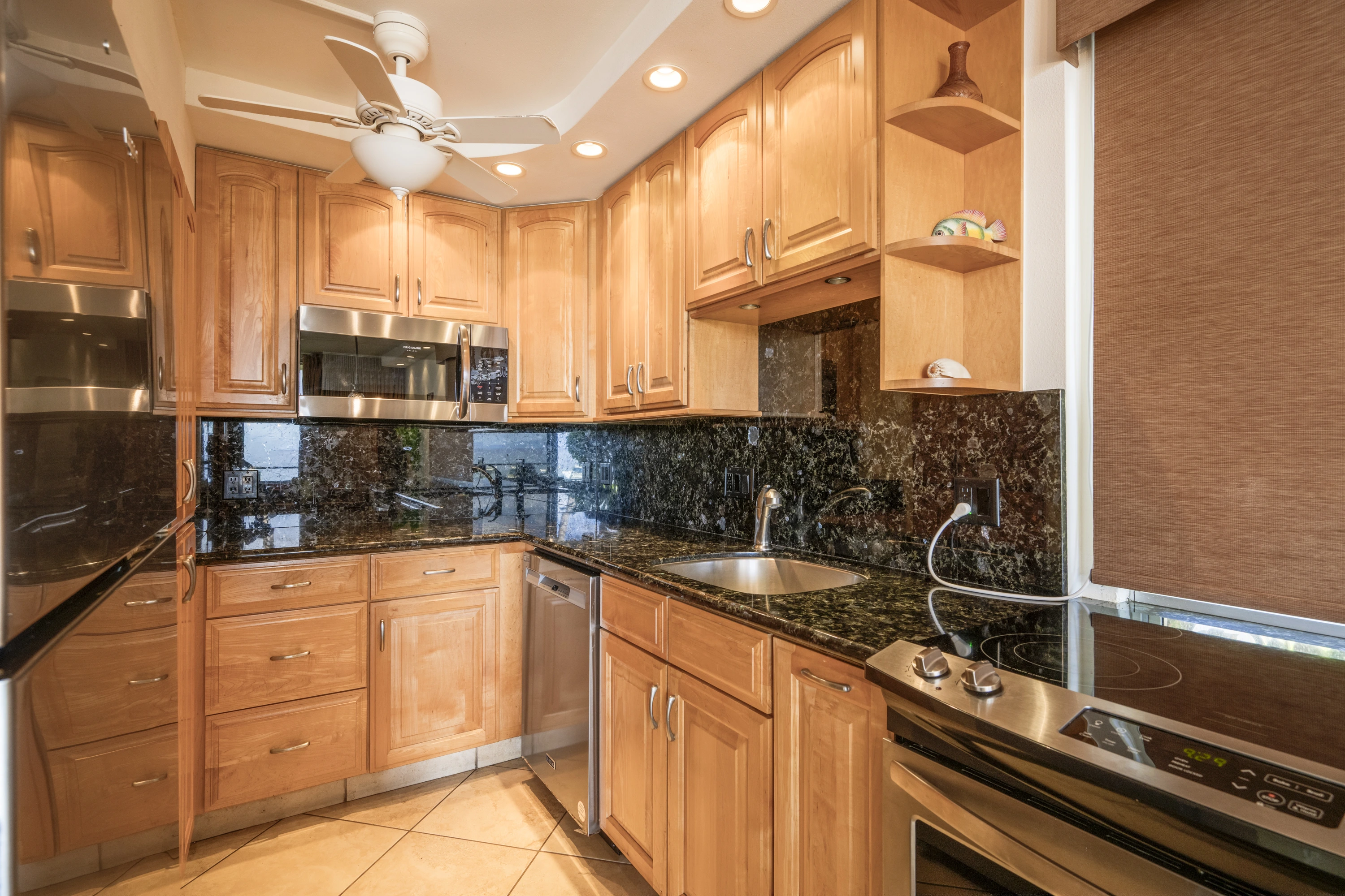 Kitchen with wood cabinets, dark counters and tiled backsplash.