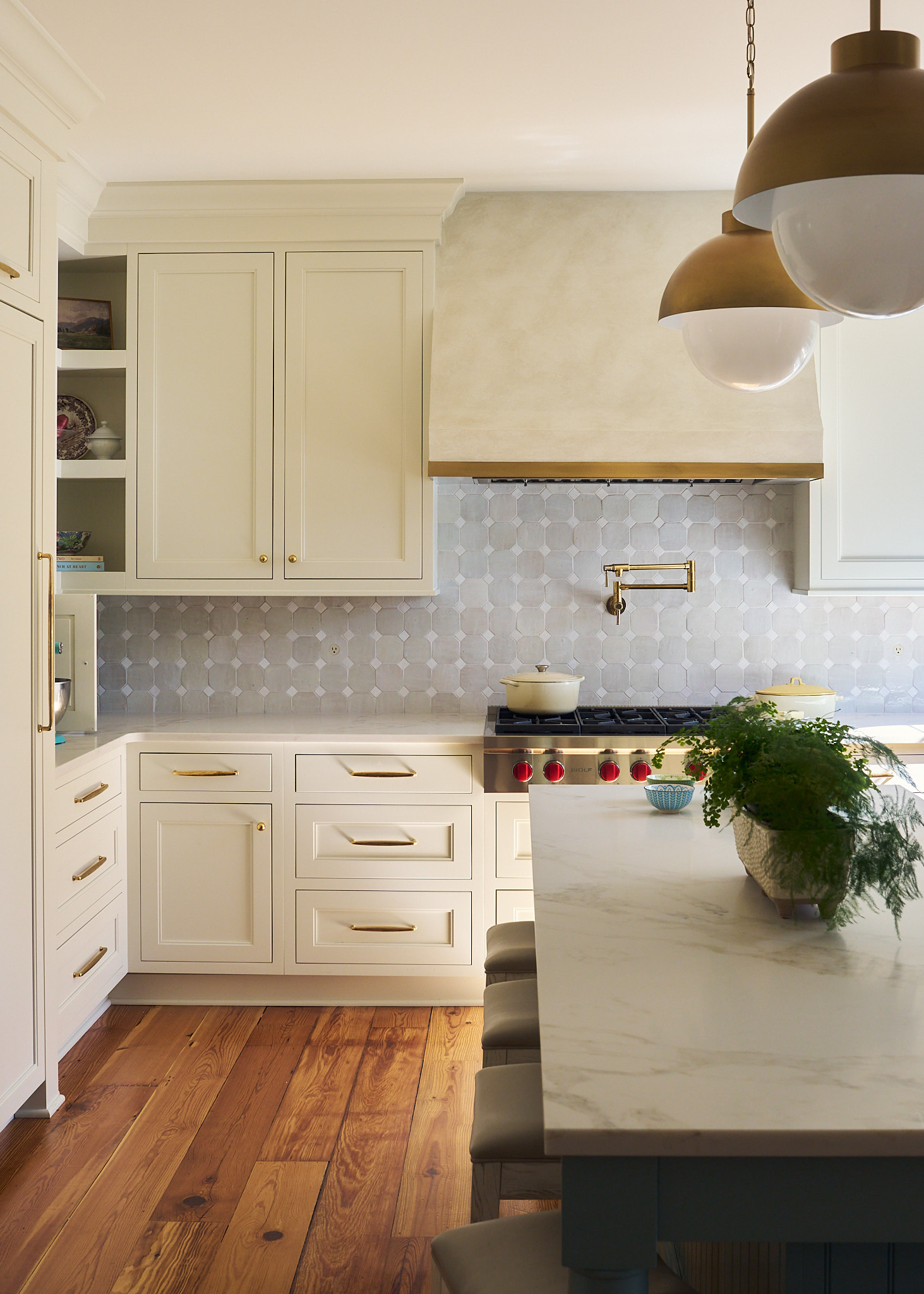 Bright Charleston kitchen with creamy inset cabinetry, marble waterfall island, brass hardware and fixtures, hex tile backsplash, statement dome pendants, and arched window filling the space with natural light.