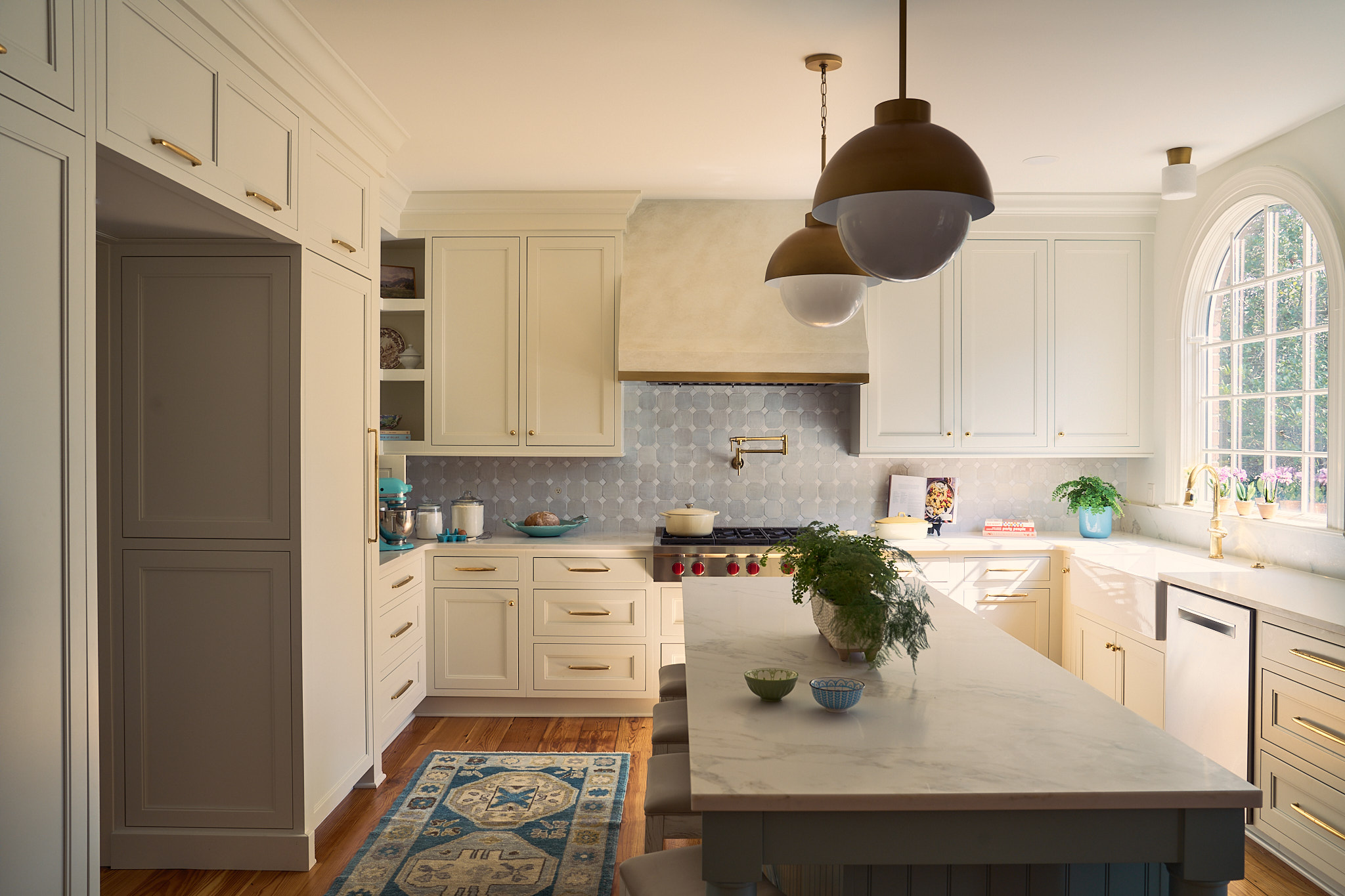 Bright, airy kitchen renovation in Hobcaw Creek featuring custom cream cabinetry, marble island, brass hardware, hex tile backsplash, and pendant lighting with natural light streaming through arched window in a Charleston South Carolina Lowcountry home