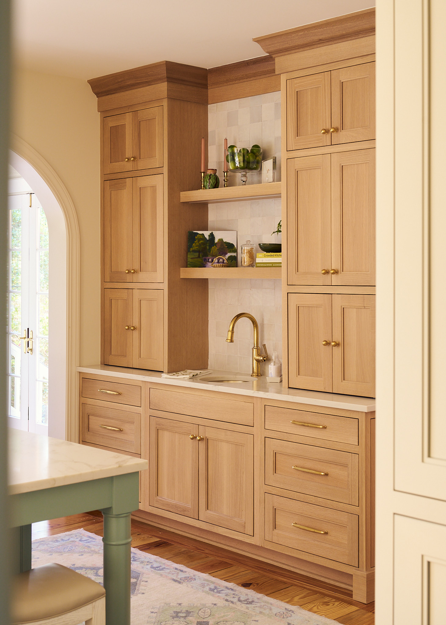 Custom white oak built-in cabinetry with brass hardware and integrated bar sink, featuring open shelving, marble countertops, and zellige tile backsplash, creating a warm and functional Charleston kitchen coffee station.