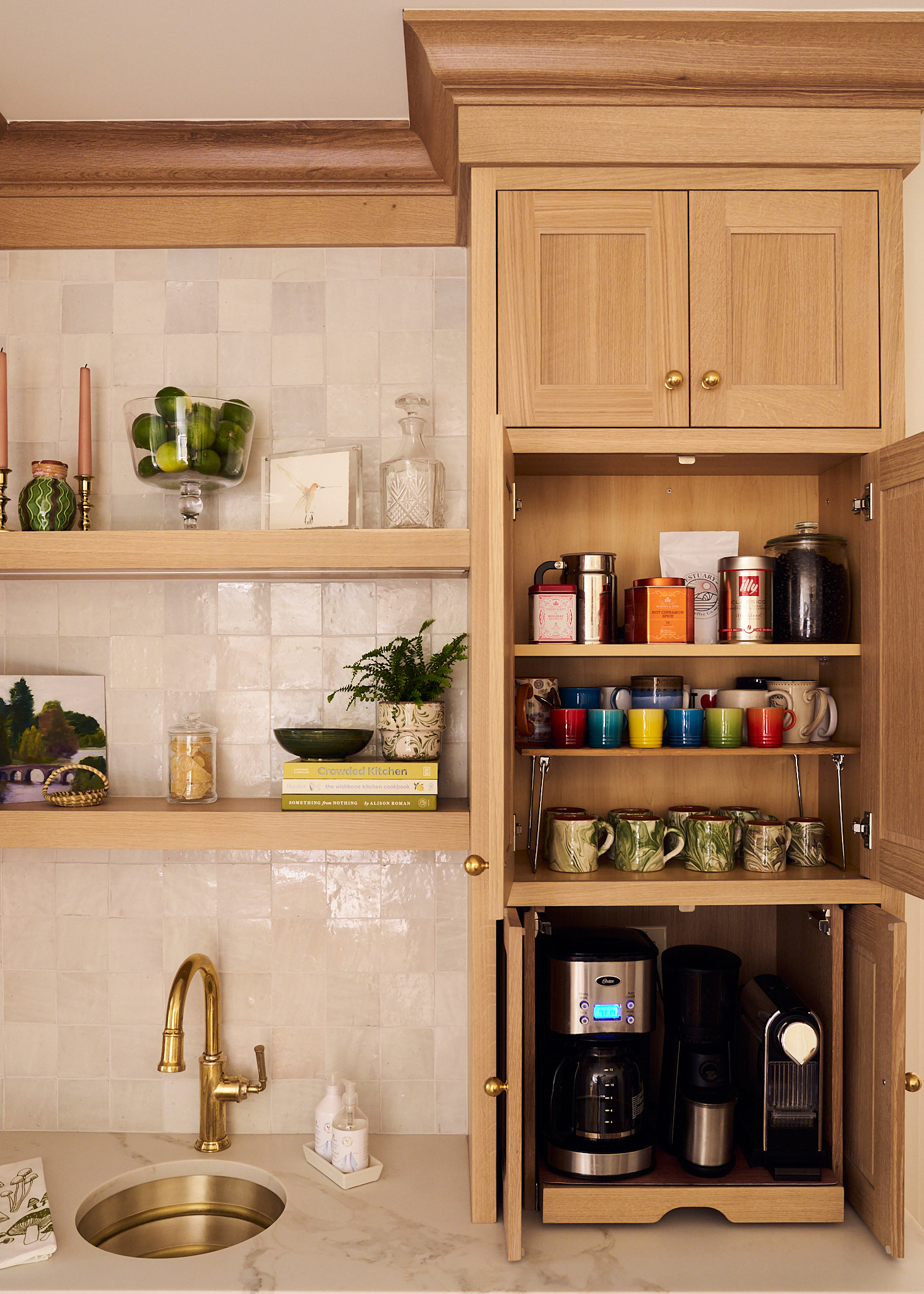 Custom white oak coffee station with built-in cabinetry and open shelving, featuring brass sink and faucet, zellige tile backsplash, styled mugs and coffee essentials, and integrated appliances for a warm, functional Charleston kitchen design.