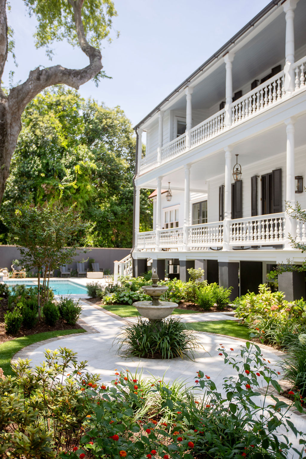 Elegant Charleston single house with expansive piazzas, traditional shutters, lush landscaping, and wrought iron fencing. Designed by PWD Studio, the property combines historic preservation with sophisticated outdoor living.