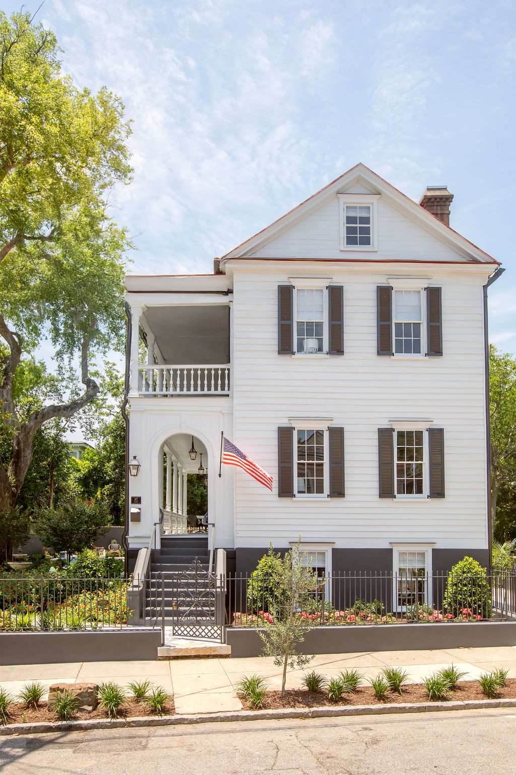 Restored historic Charleston residence featuring classic white clapboard siding, double piazzas, black shutters, and manicured gardens. Designed by PWD Studio, the home celebrates timeless Southern architecture and Lowcountry living.