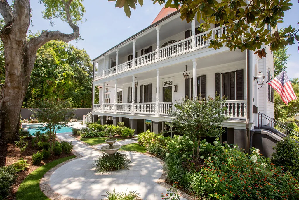 Restored Charleston single house with double piazzas, manicured garden courtyard, brick pathways, fountain, and resort-style pool showcasing timeless Southern architecture and historic preservation.