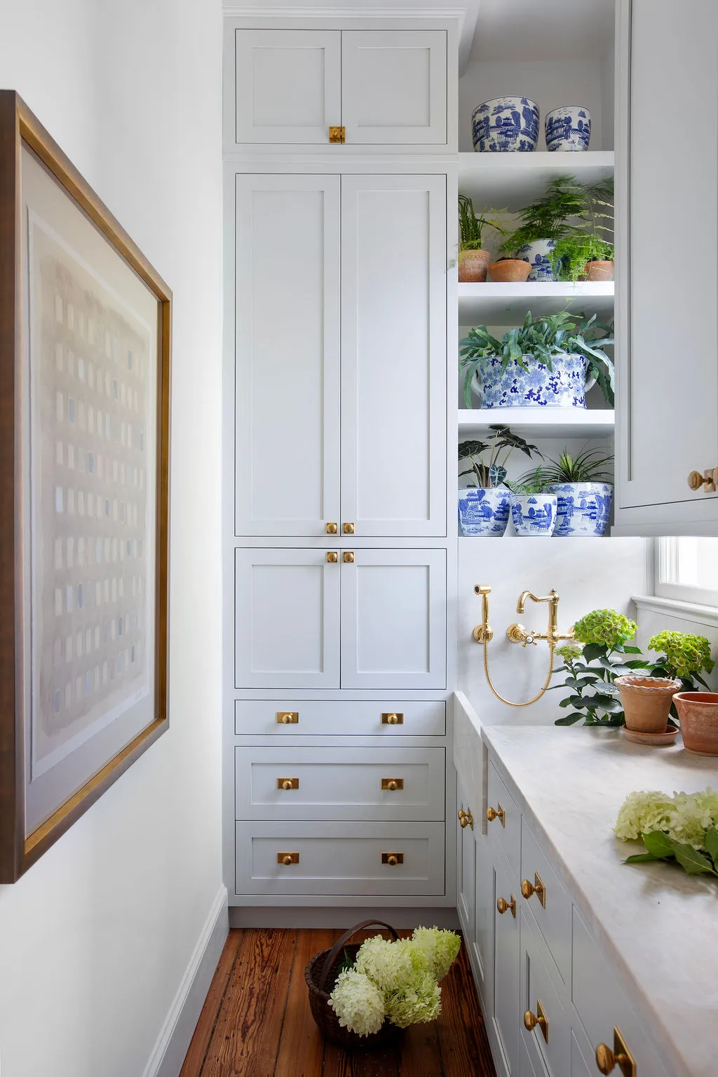 Custom butler’s pantry featuring floor-to-ceiling gray cabinetry, marble countertops, unlacquered brass fixtures, and blue-and-white porcelain planters. Designed by PWD Studio, this Charleston home showcases tailored millwork, functional storage, and timel