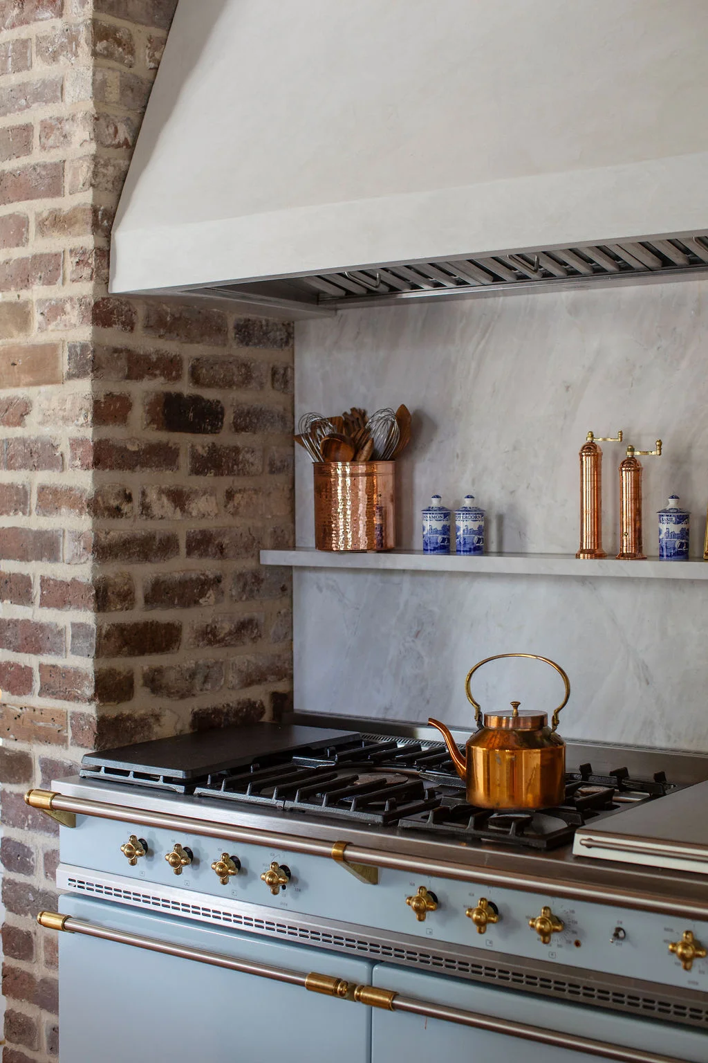 Luxury kitchen featuring exposed brick walls, reclaimed wood ceilings, a custom walnut island, marble countertops, and a professional range framed by a plaster hood. Designed by PWD Studio, the space blends historic Charleston character with timeless craft