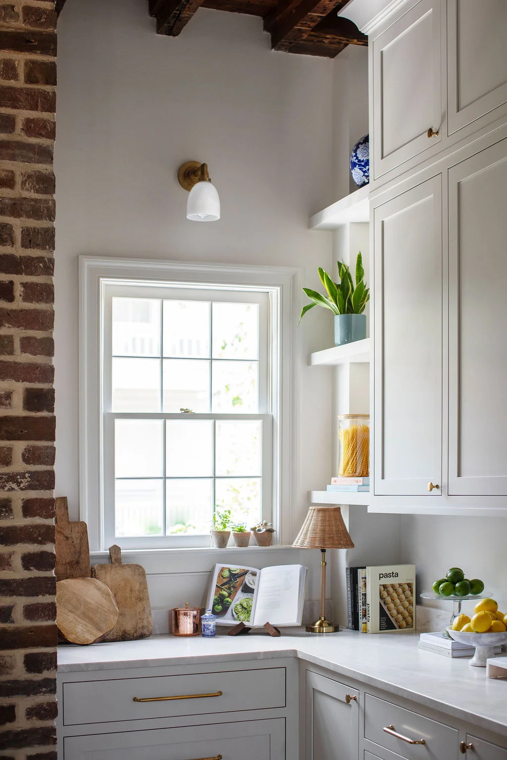 Custom kitchen corner featuring light gray cabinetry, marble countertops, open shelving, brass hardware, and collected culinary accessories. Designed by PWD Studio, this Charleston interior showcases thoughtful storage and timeless craftsmanship.