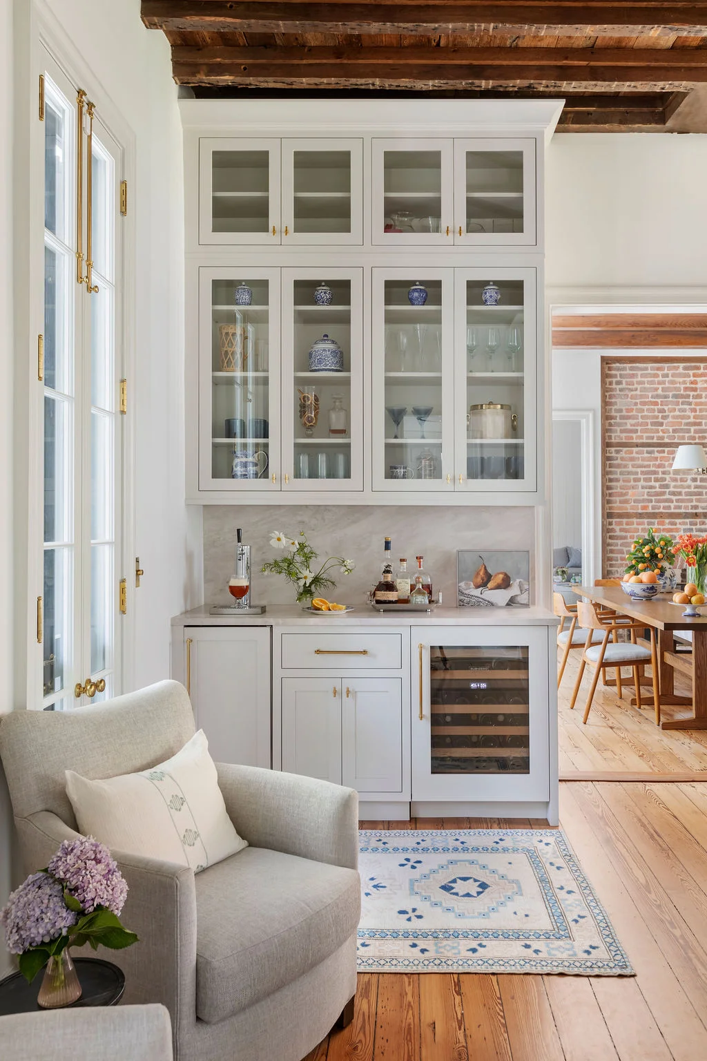 Elegant butler’s pantry featuring glass-front cabinetry, marble countertops, a built-in wine refrigerator, and unlacquered brass hardware. Designed by PWD Studio, the space combines functional entertaining storage with timeless Charleston design.