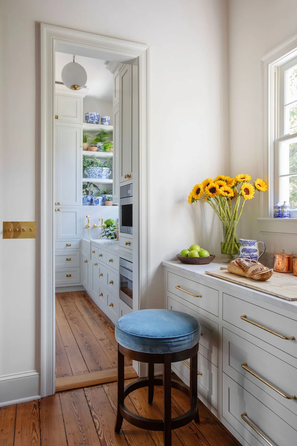 Elegant butler’s pantry with custom light gray cabinetry, unlacquered brass hardware, open shelving, and antique pine flooring. Designed by PWD Studio, the space balances refined storage, timeless materials, and sophisticated Southern design.