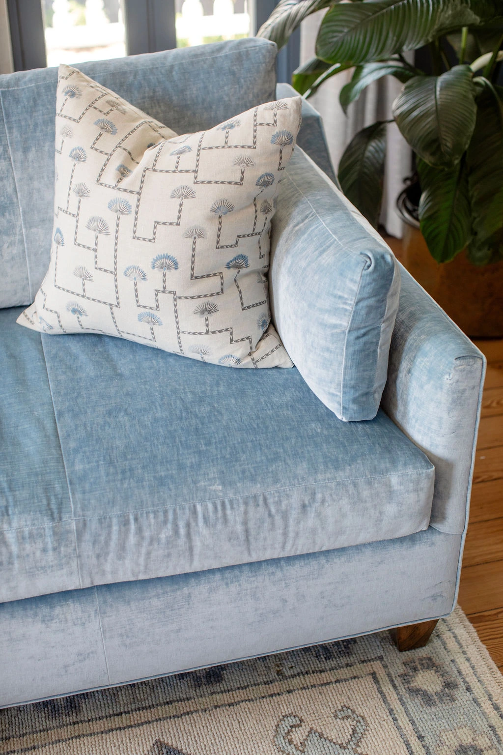 Close-up of a custom light blue velvet sofa with a tailored decorative pillow in a soft blue geometric floral pattern. Designed by PWD Studio, the vignette highlights layered textiles, luxury upholstery, and timeless coastal-inspired interiors with an eleg