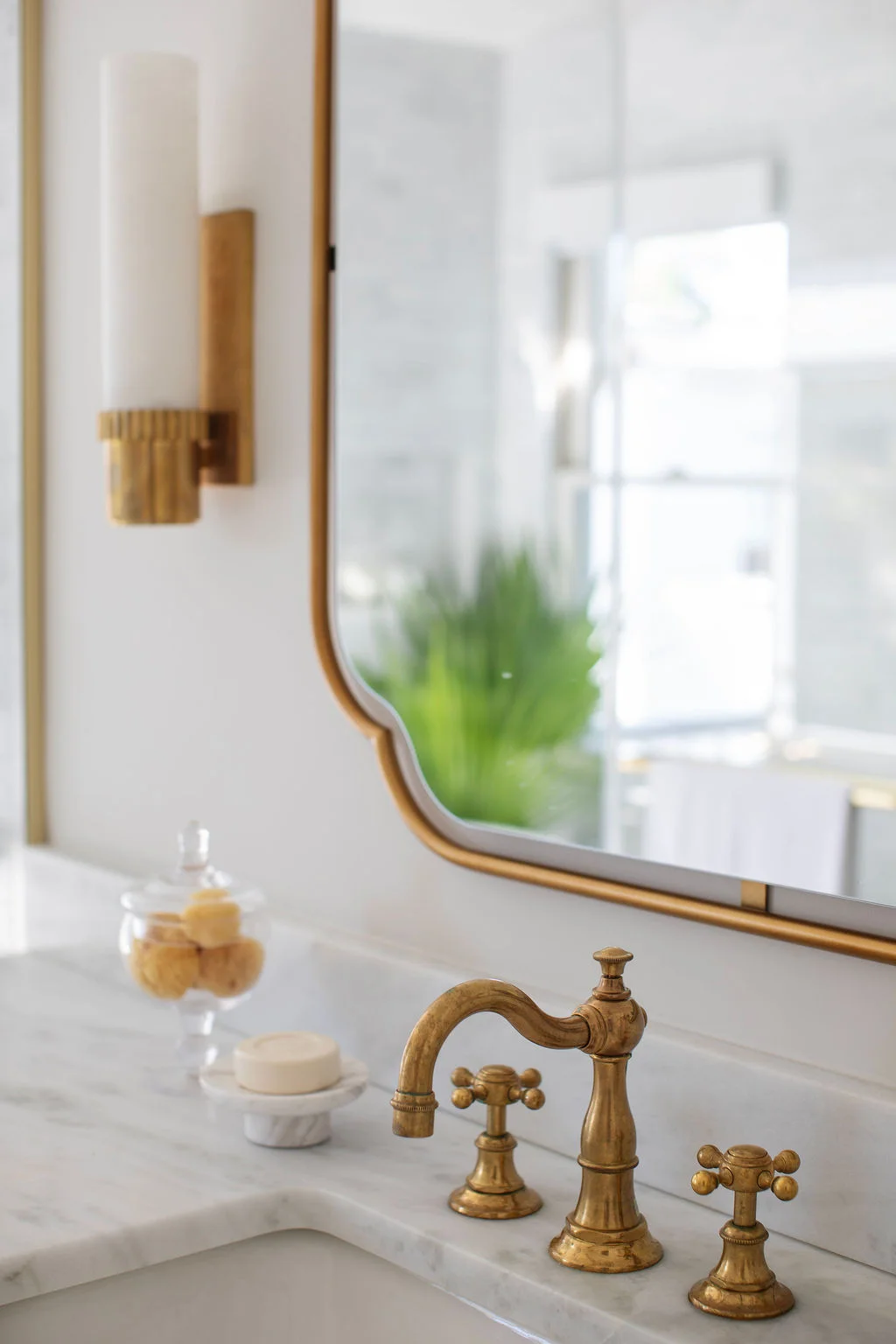 Luxury bathroom vanity with marble countertops, unlacquered brass faucet, custom mirror, and refined brass lighting. Designed by PWD Studio, the space blends classic materials, tailored detailing, and timeless elegance.