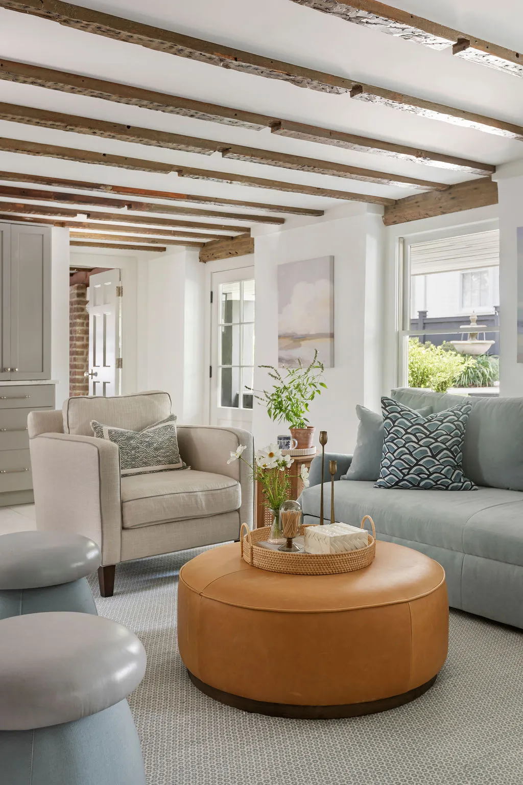 Inviting family room with exposed reclaimed wood ceiling beams, custom pale blue sofa, leather ottoman coffee table, and tailored neutral seating. Designed by PWD Studio, this Charleston interior balances historic character with relaxed modern comfort.