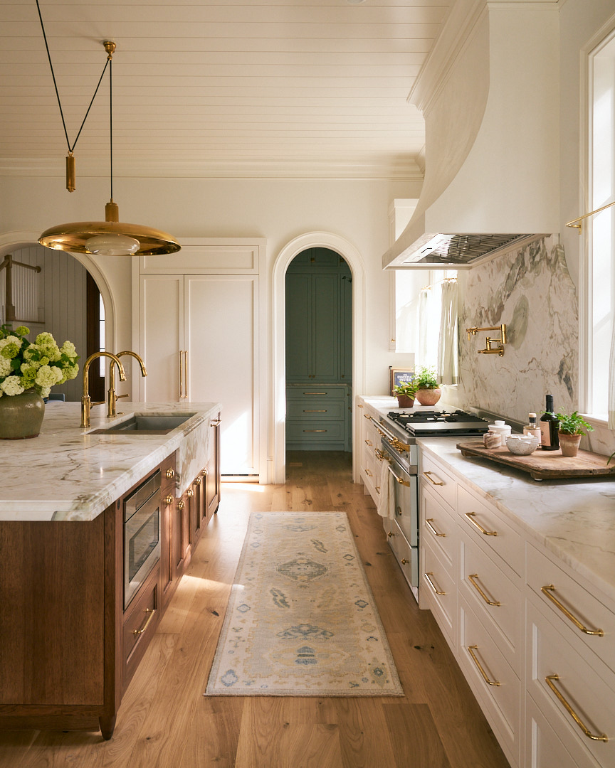 Luxury Kiawah Island kitchen with a walnut island, marble countertops, custom plaster range hood, brass fixtures, and a dramatic veined stone backsplash designed for entertaining.