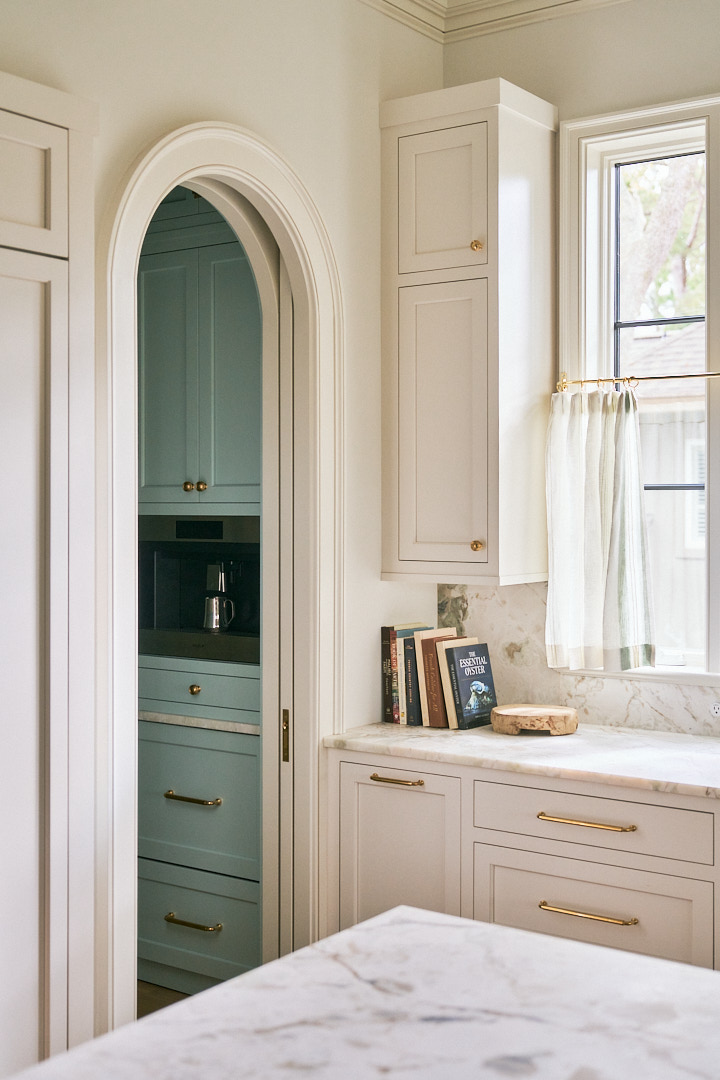 Custom kitchen with marble countertops, brass hardware, and an arched opening leading to a soft blue scullery with integrated coffee station in a luxury Kiawah Island residence.