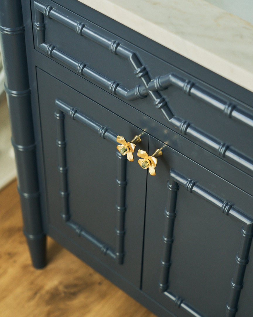 Custom navy vanity with bamboo-inspired millwork, whimsical brass butterfly hardware, and marble countertop showcasing bespoke craftsmanship in a luxury powder room.