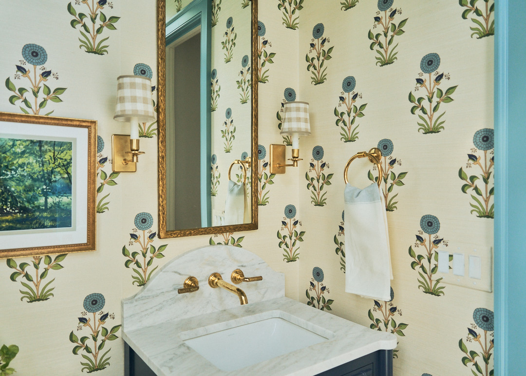Powder room with floral wallpaper, sky-blue trim, and a distinctive oval window framing natural light in a thoughtfully designed Kiawah Island residence.