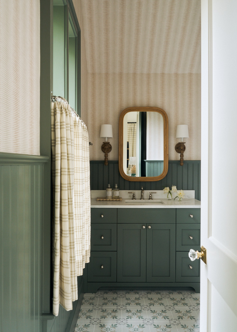 Charming bathroom with sage green beadboard wainscoting, patterned tile flooring, custom vanity, and warm wood-framed mirror in a Kiawah Island retreat.