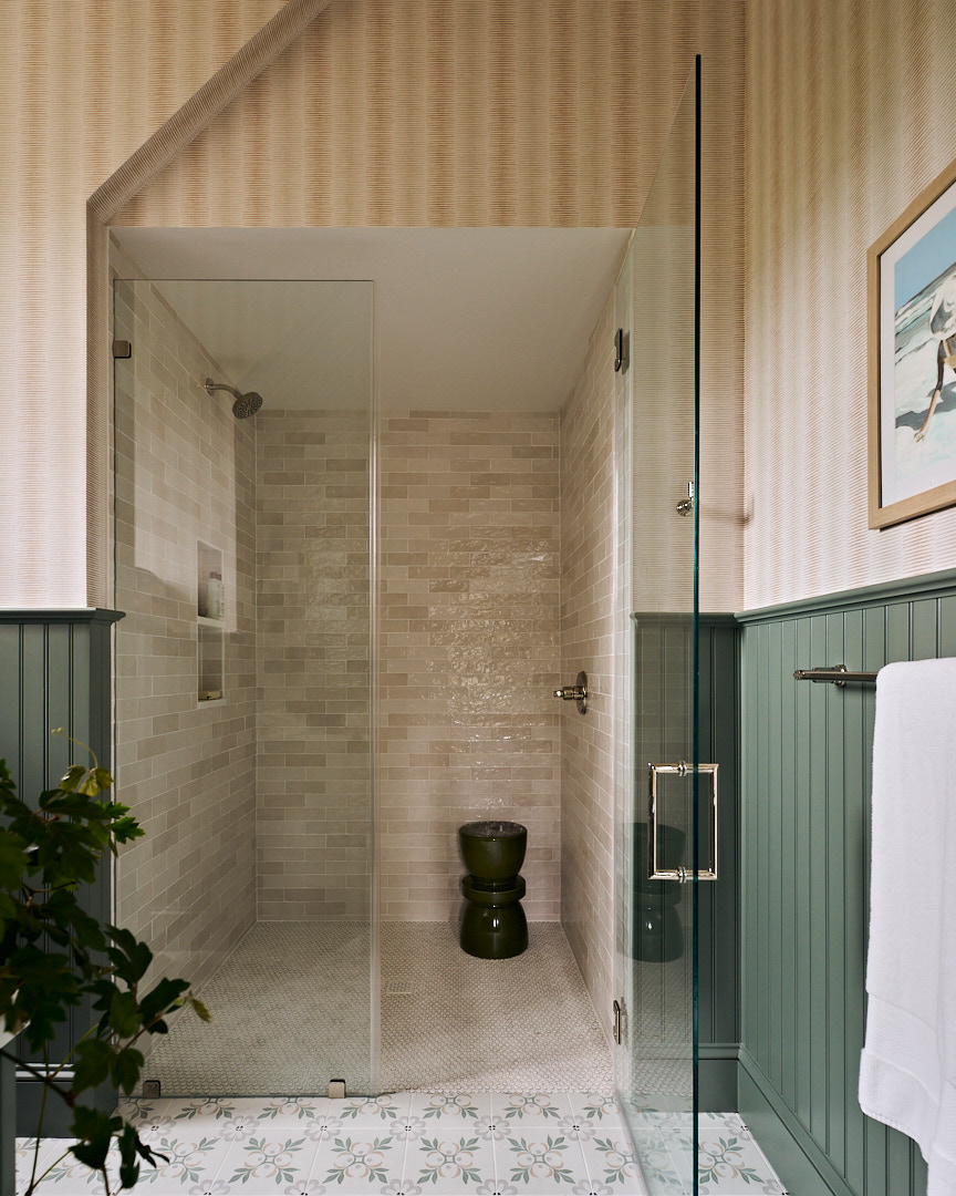 Custom bathroom with sage green beadboard walls, patterned floor tile, and a glass-enclosed shower finished with handcrafted ceramic tile.