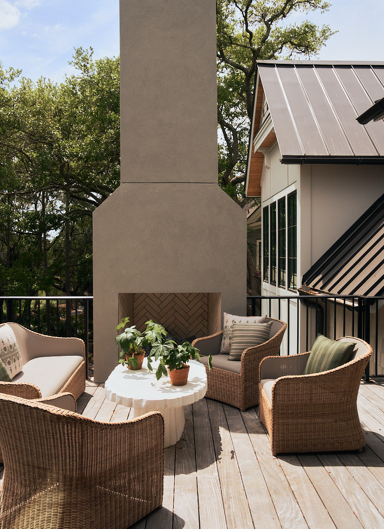 Luxury Kiawah Island outdoor living terrace with woven lounge seating, a custom stucco fireplace, metal roof detailing, and elevated views of the surrounding golf course and maritime forest.