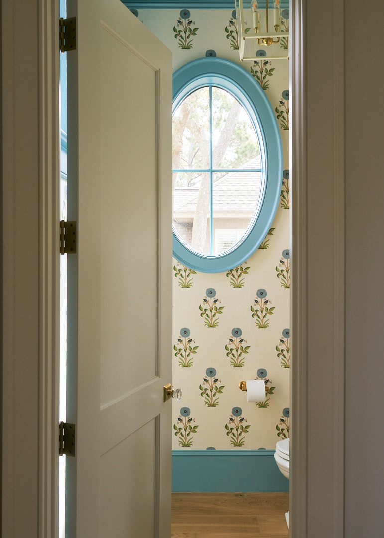 Custom powder room featuring botanical wallpaper, a marble backsplash, brass faucet, decorative mirror, and layered traditional details in a Kiawah Island home.