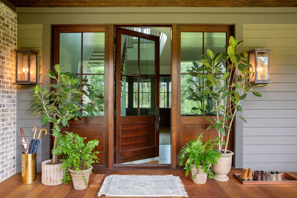 Luxury Lowcountry home entry by PWD Studio featuring custom wood and glass doors, brick and horizontal siding, brass lanterns, layered greenery, and a welcoming covered porch.