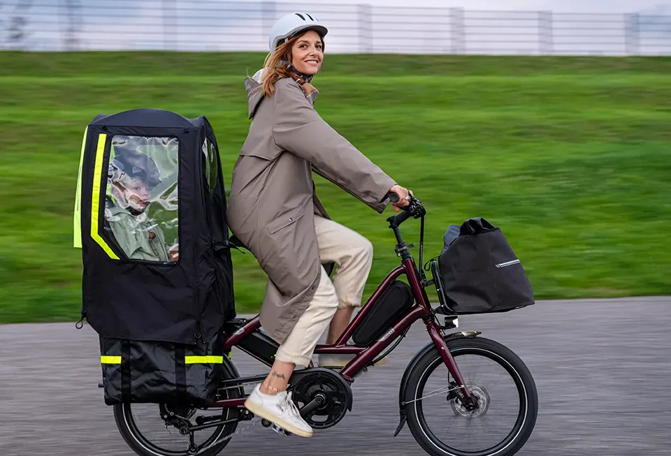 Red Tern cargo bike with a child seat, a woman wearing a helmet riding on a green bike path