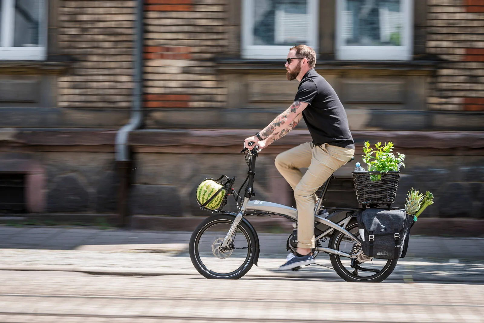 Silver Tern folding bike with a black basket; a cyclist on a cobblestone street in front of brick buildings