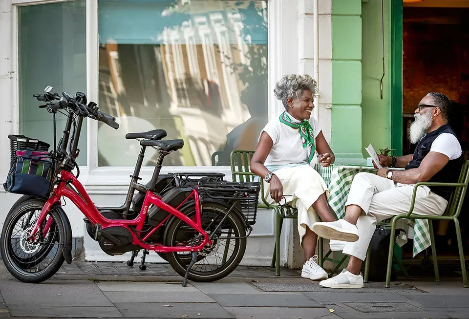 A red Tern e-bike with a basket, parked in front of a café