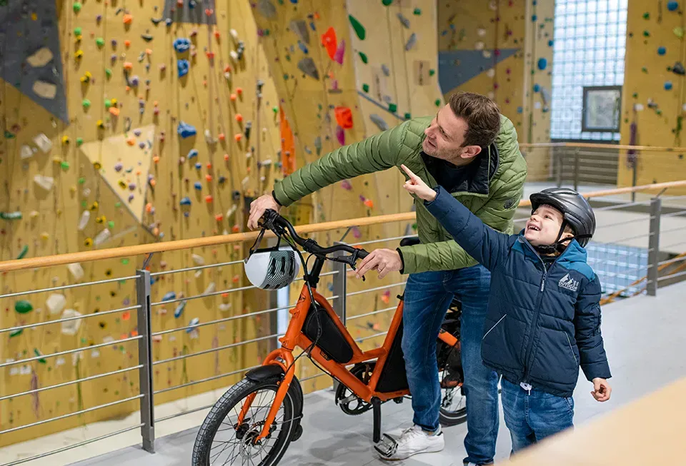 Orange Tern cargo bike in a climbing gym with a man and a child in winter gear