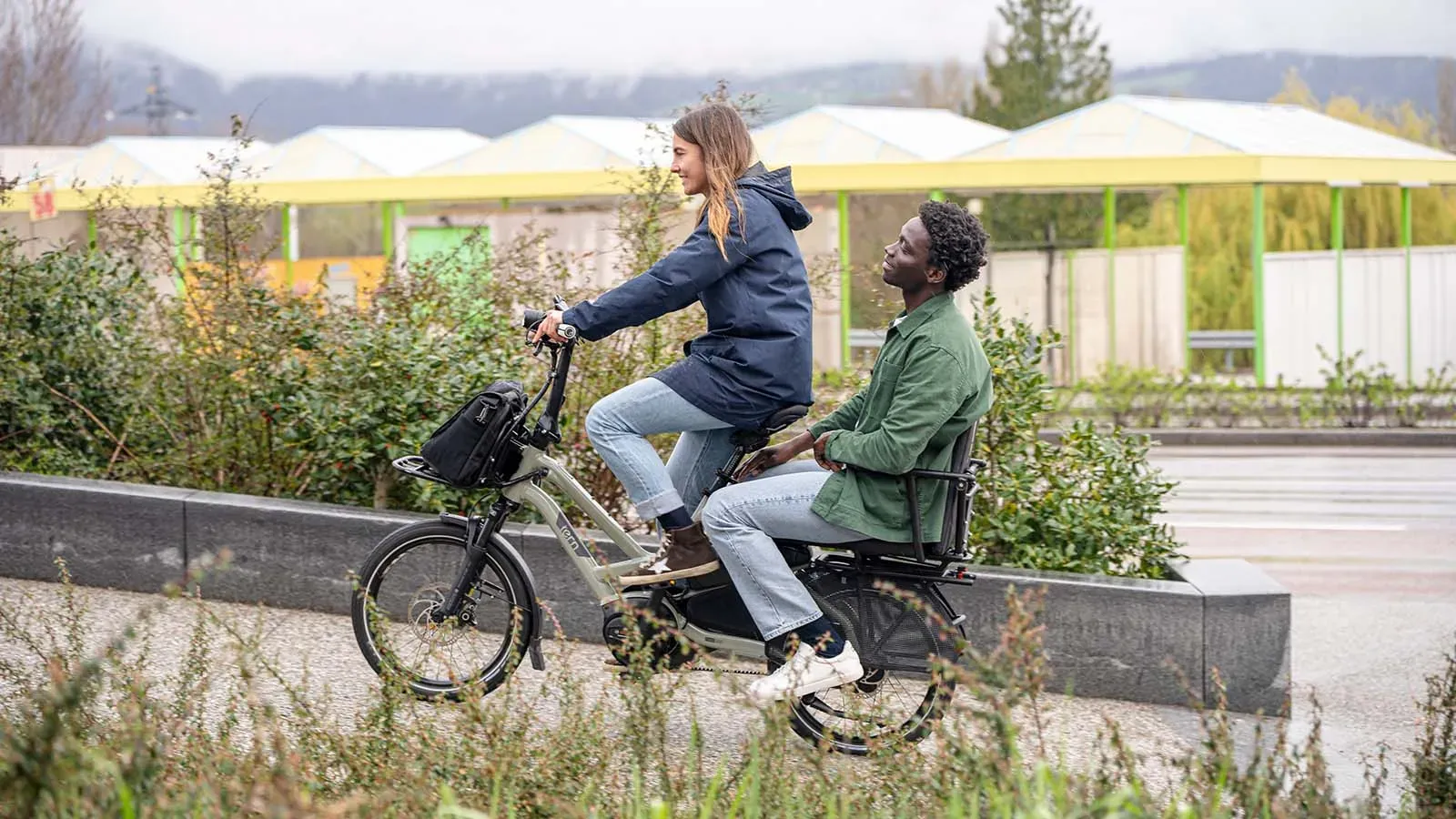 Gray Tern cargo bike with two passengers, sturdy frame in a green urban setting
