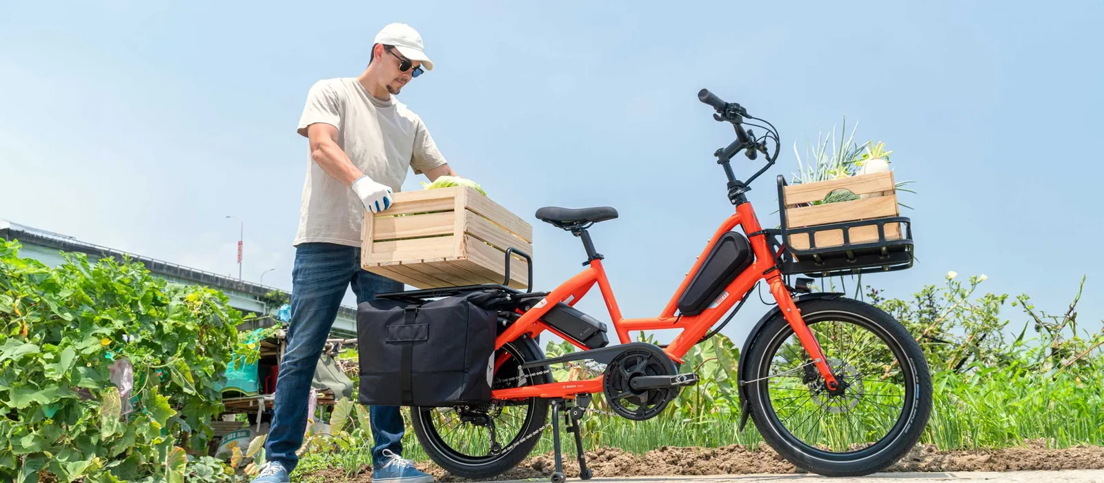 Orange Tern cargo bike with wooden baskets and a sturdy frame, with a man in the background