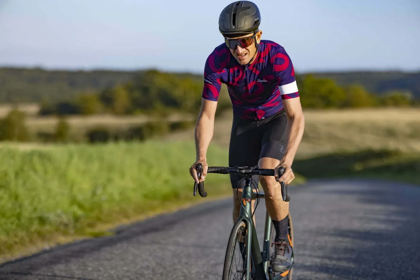 Road cyclist riding a Principia bike, black frame, with a green countryside in the background