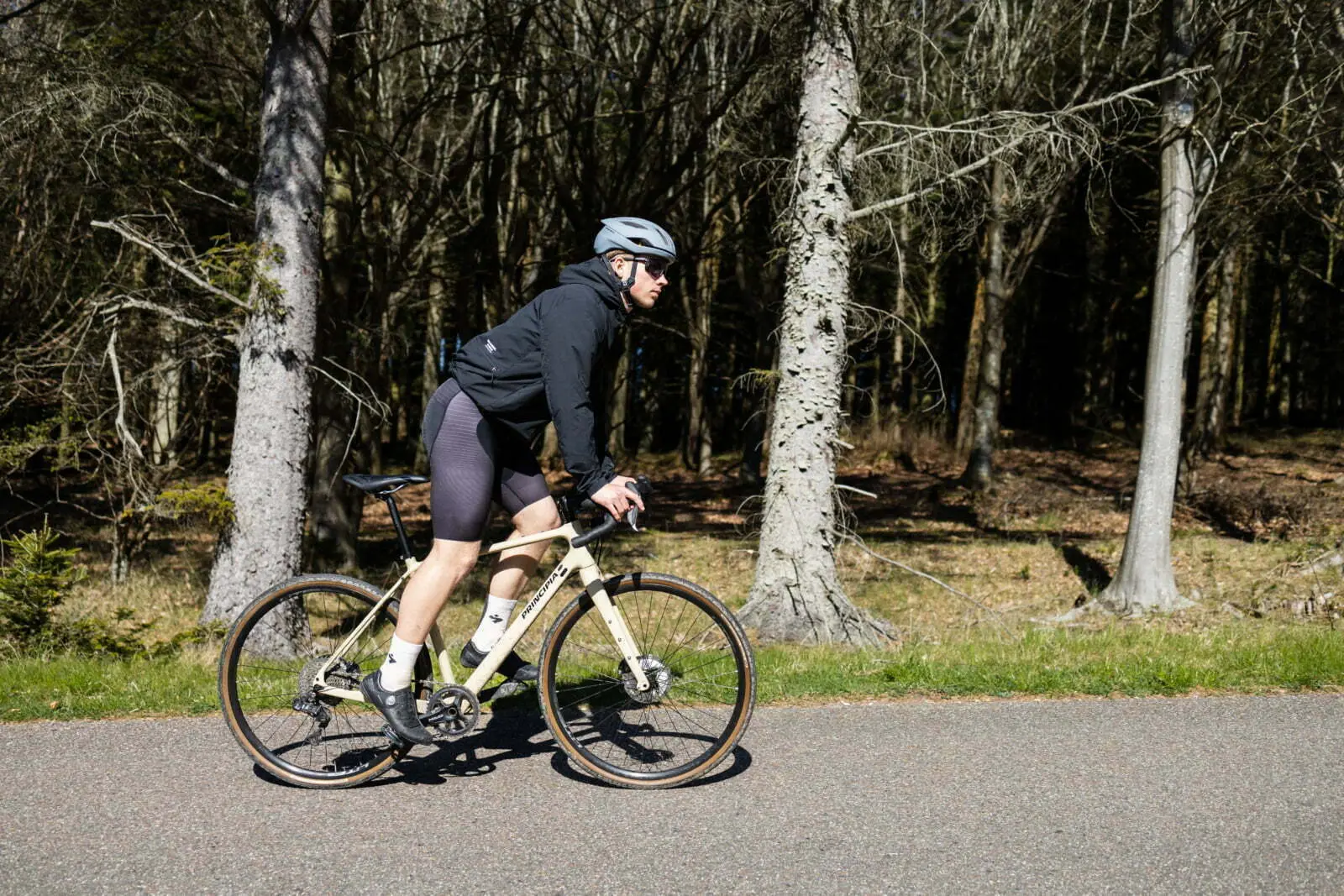 A beige Principia road bike riding on a forest road with a cyclist in black clothing