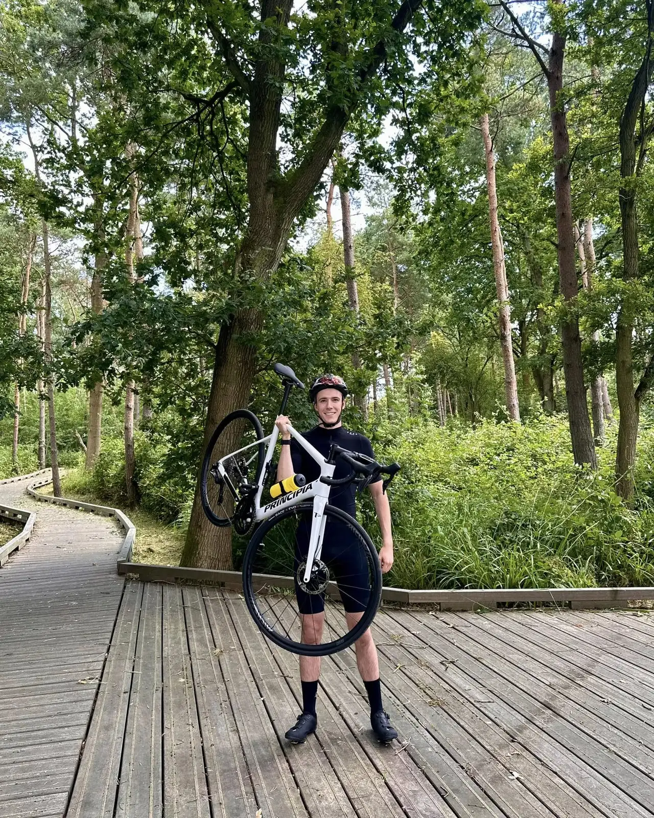 A white Principia road bike on a wooden bridge in a lush forest