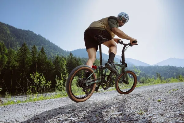 Green Brompton folding bike in the mountains; cyclist wearing a helmet on a gravel path