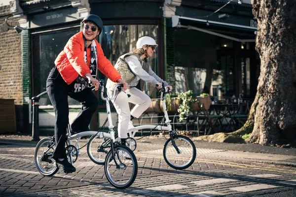Gray Brompton folding bikes in action on a city street, with cyclists wearing helmets