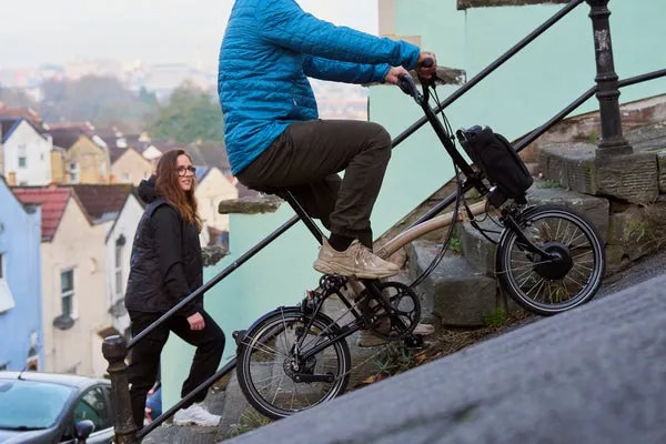A black Brompton folding bike being ridden up an urban flight of stairs