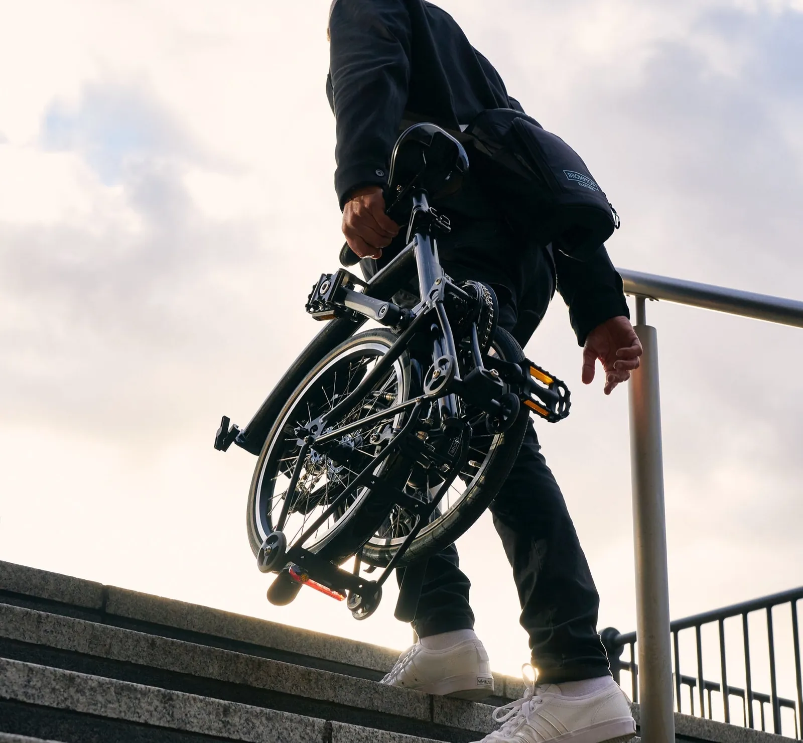 A black Brompton folding bike being carried up outdoor stairs by a cyclist