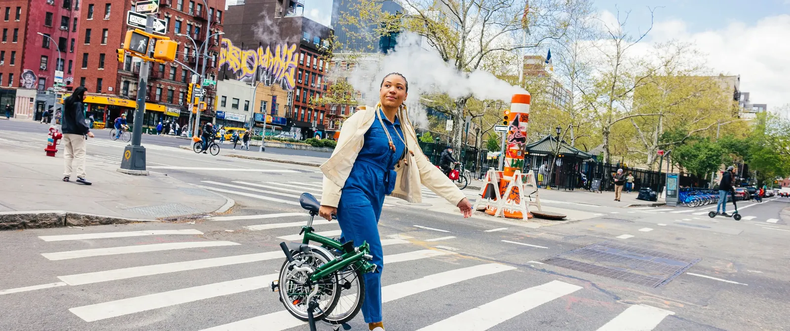 A green Brompton folding bike ridden by a woman at a busy urban intersection