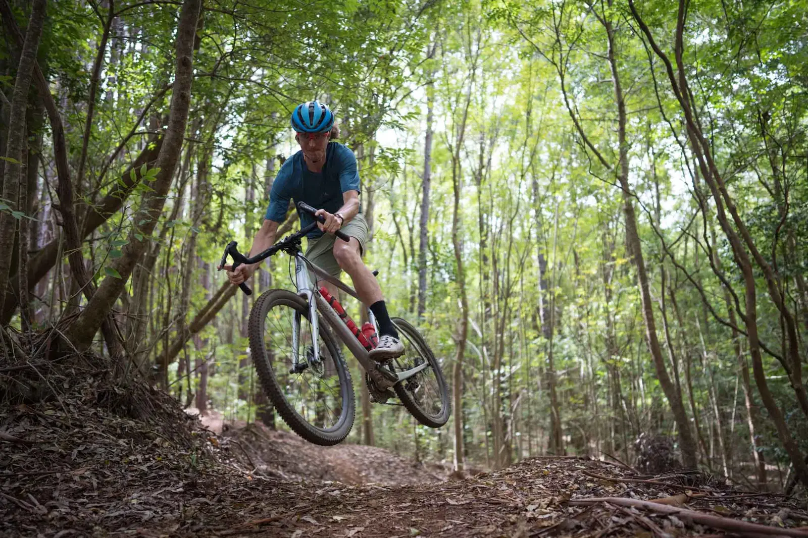 Gray Kona mountain bike on a forest trail; cyclist wearing a blue helmet in action