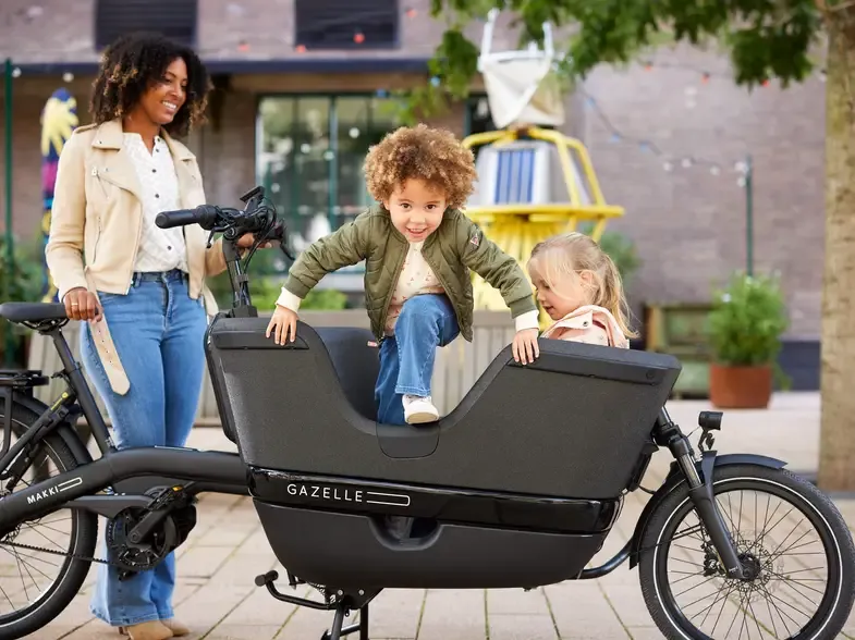 Vélo cargo noir Gazelle avec enfants assis à l'avant sur une place pavée