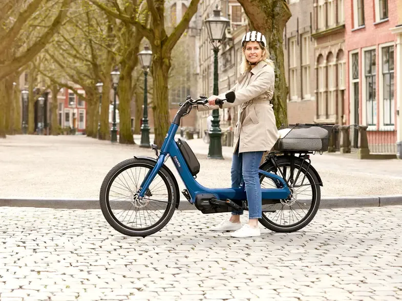 Vélo électrique Gazelle bleu avec cadre bas sur rue pavée et arbres