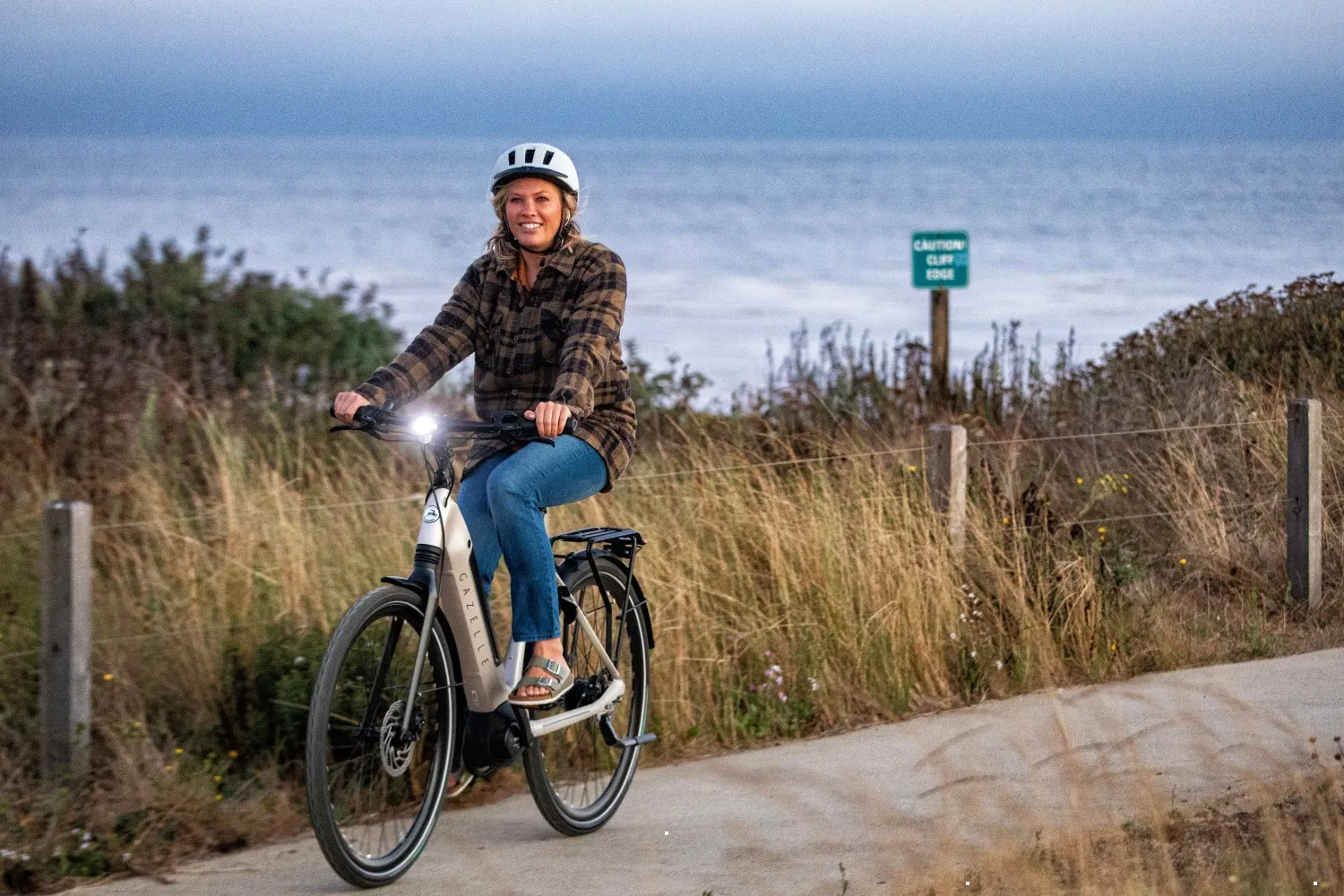 Vélo électrique Gazelle noir et gris sur piste côtière avec cycliste souriante et mer en arrière-plan
