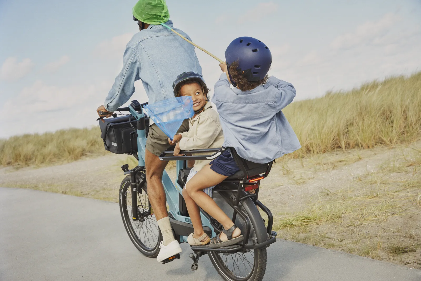 Vélo cargo Gazelle bleu dans un paysage côtier avec deux enfants à l'arrière