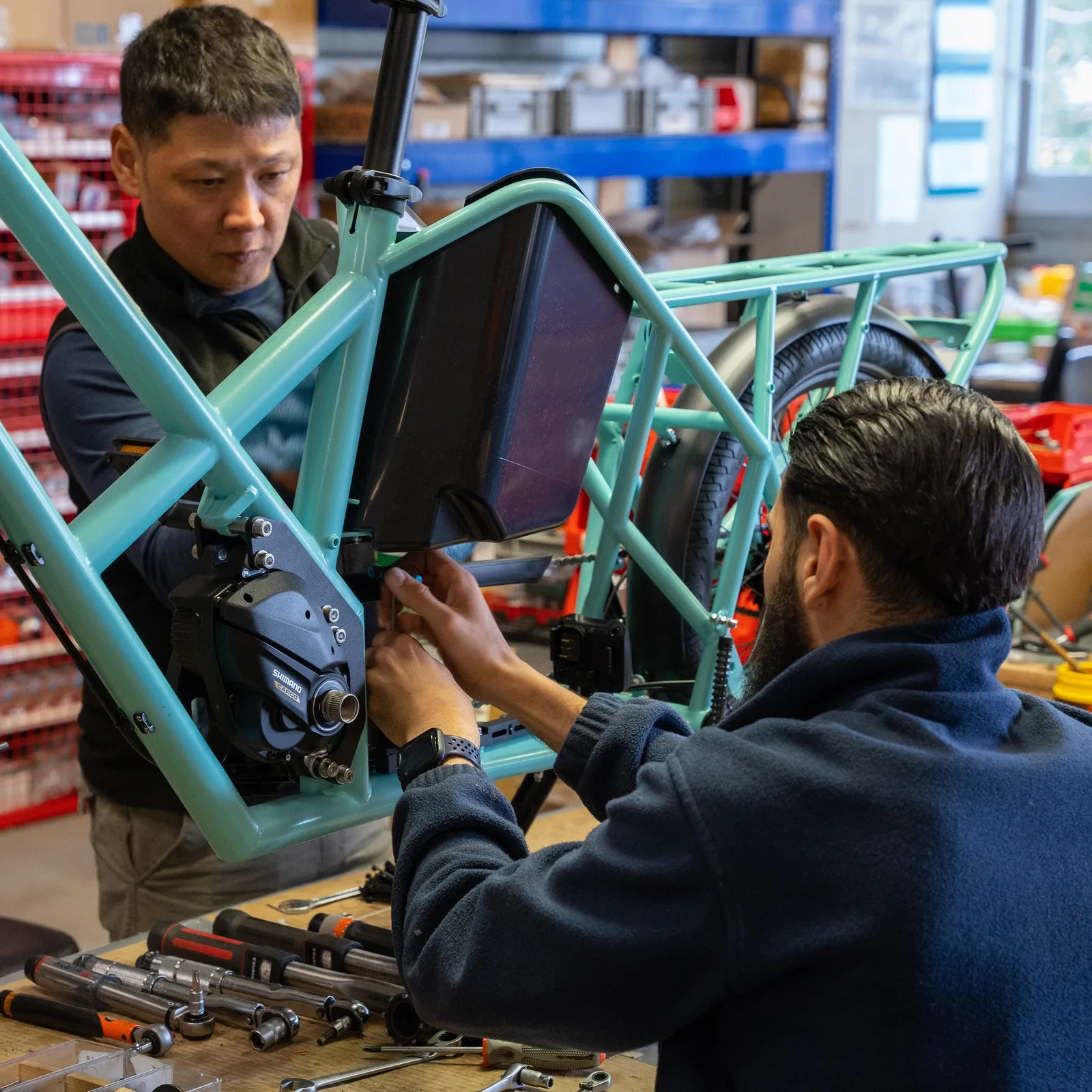 A turquoise Bike 43 cargo bike being assembled in a workshop