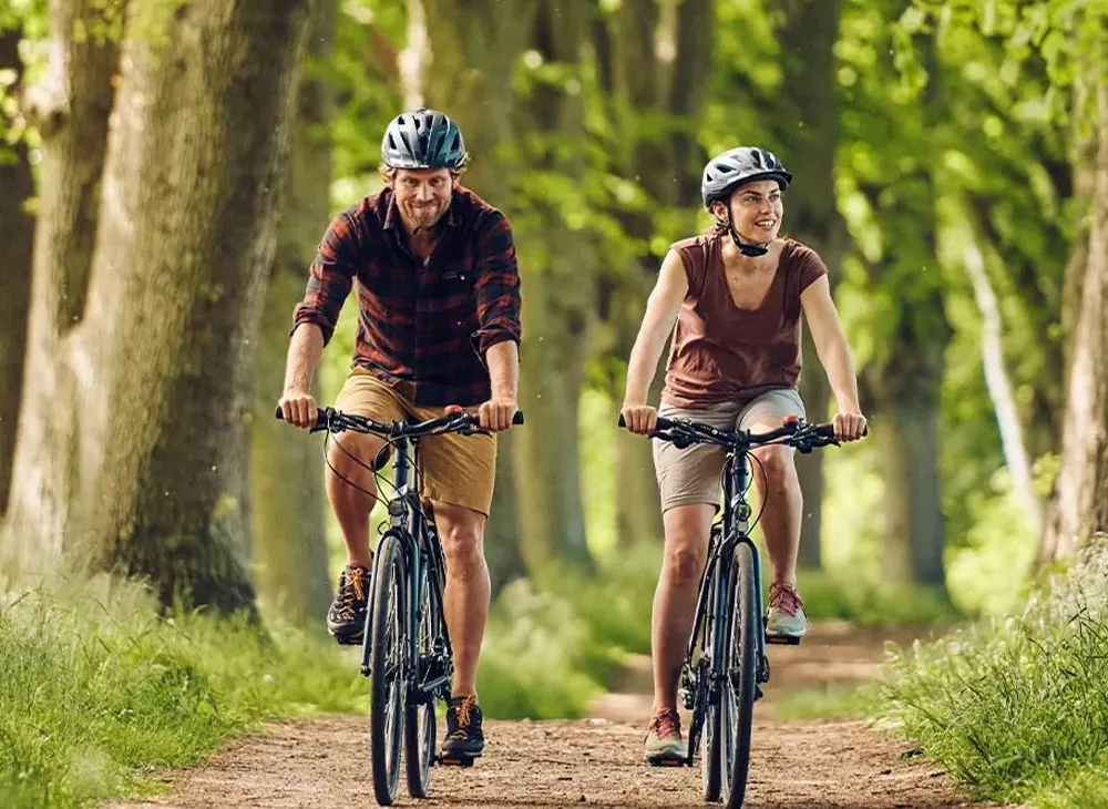 Two cyclists on black VSF Fahrradmanufaktur bicycles, with a lush forest in the background