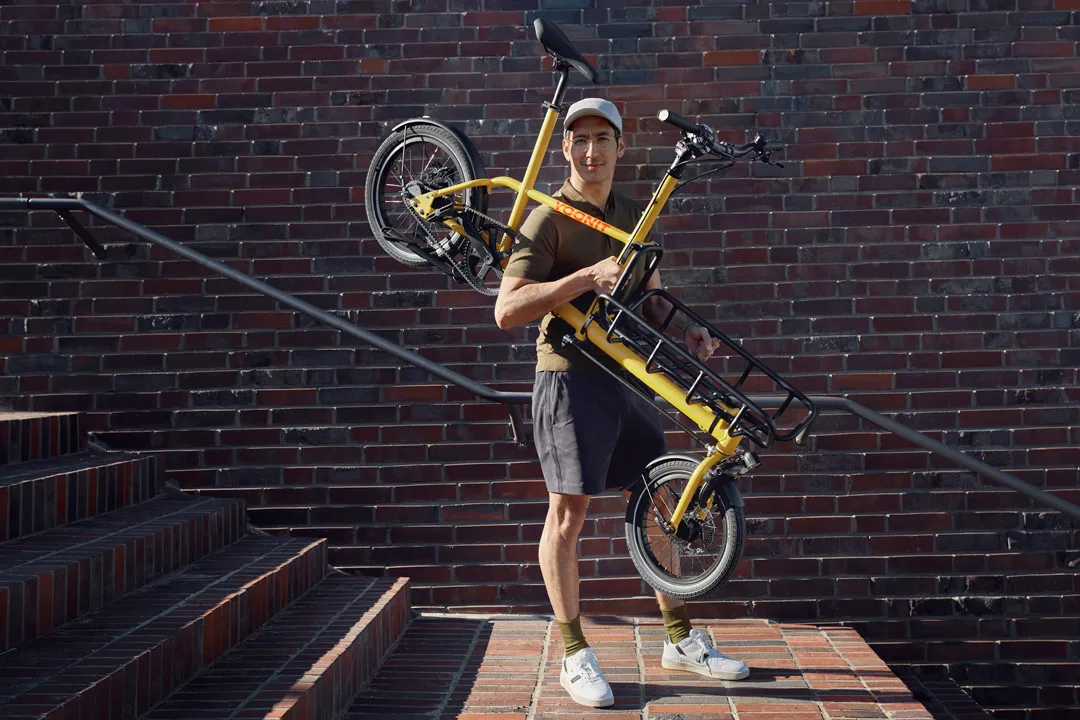 A yellow Yoonit cargo bike being ridden by a man on brick steps