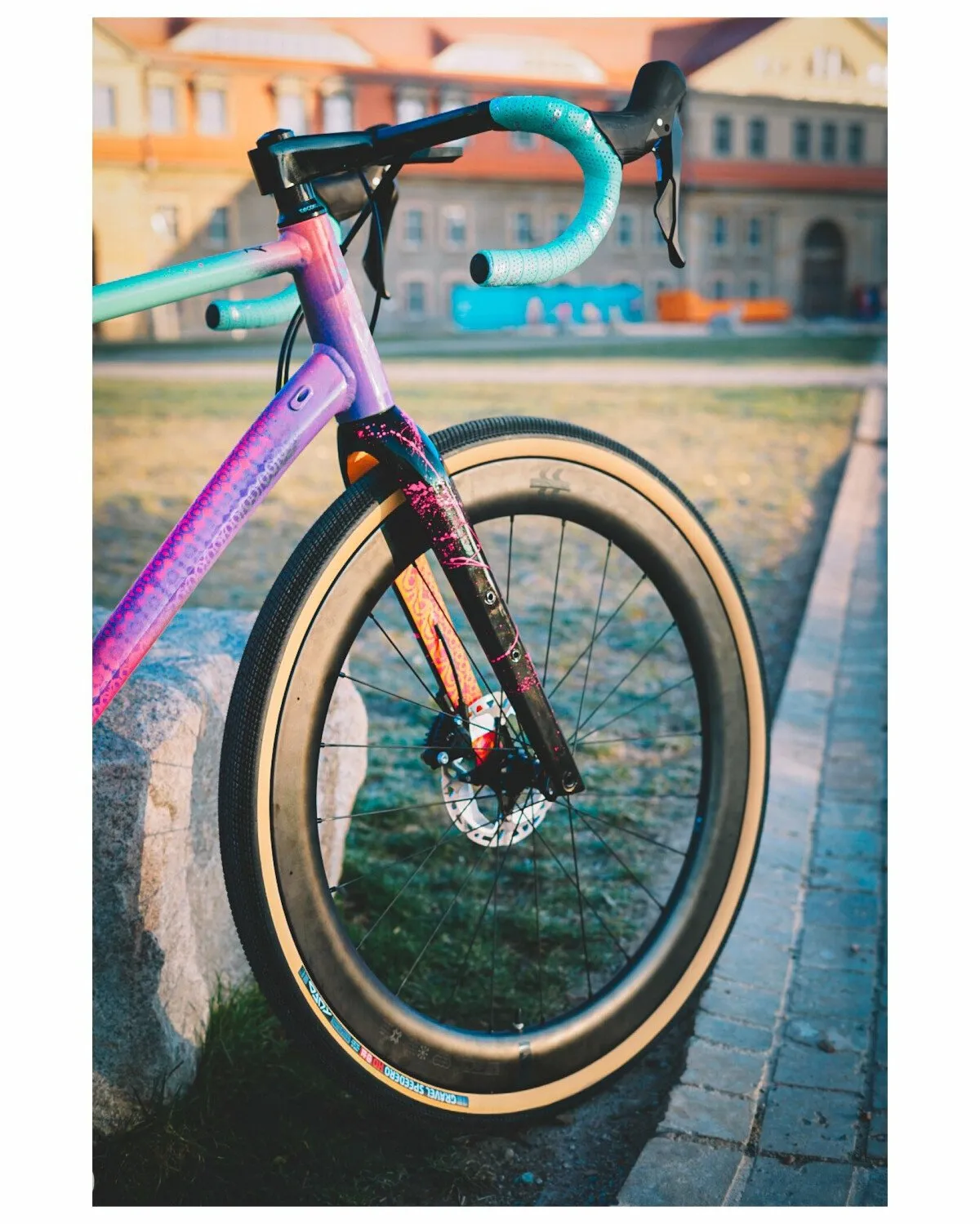A colorful Intec bike with turquoise handlebars, a purple frame, and wide tires in front of a historic building