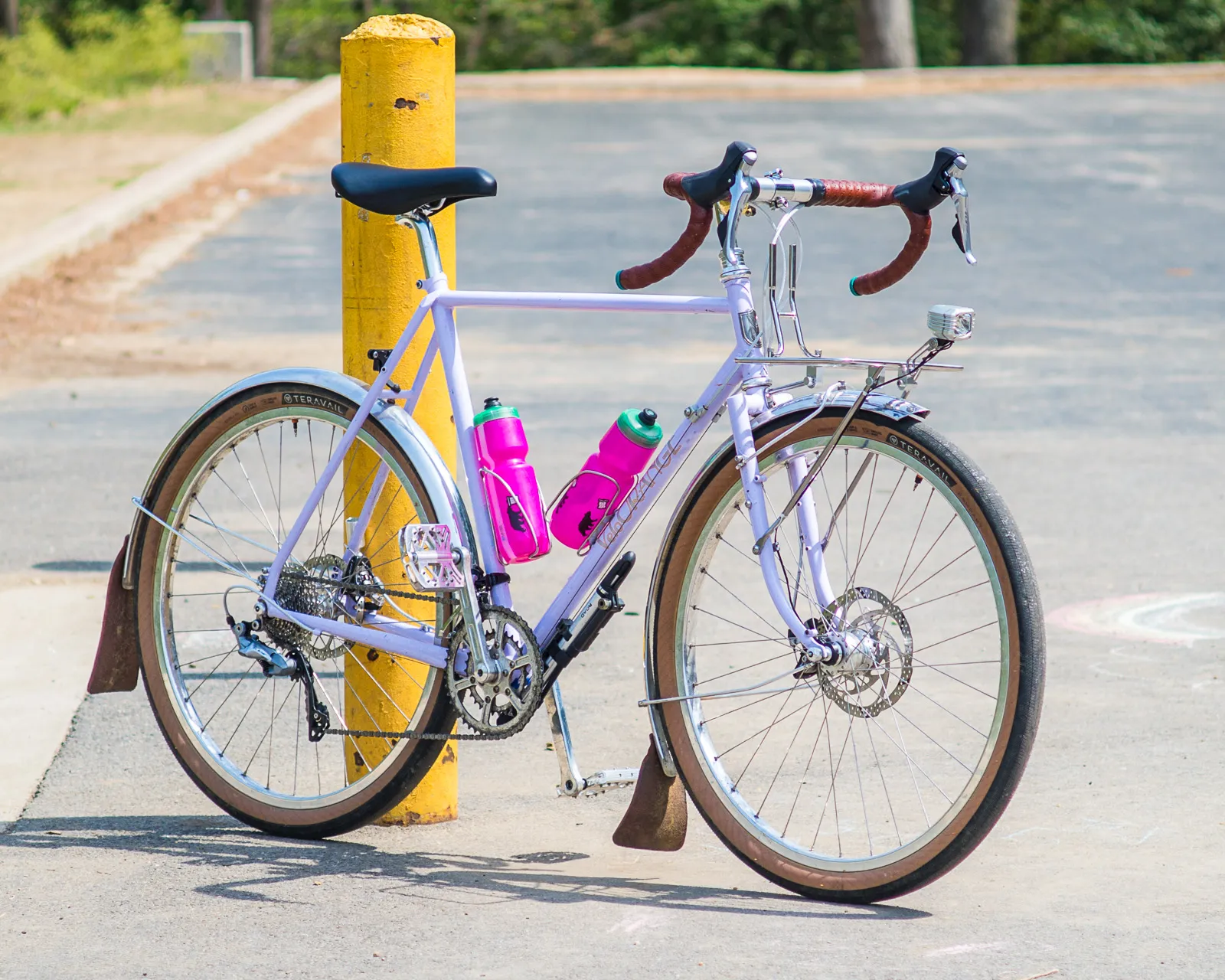 Intec road bike in purple with brown handlebars and a rack on a paved parking lot